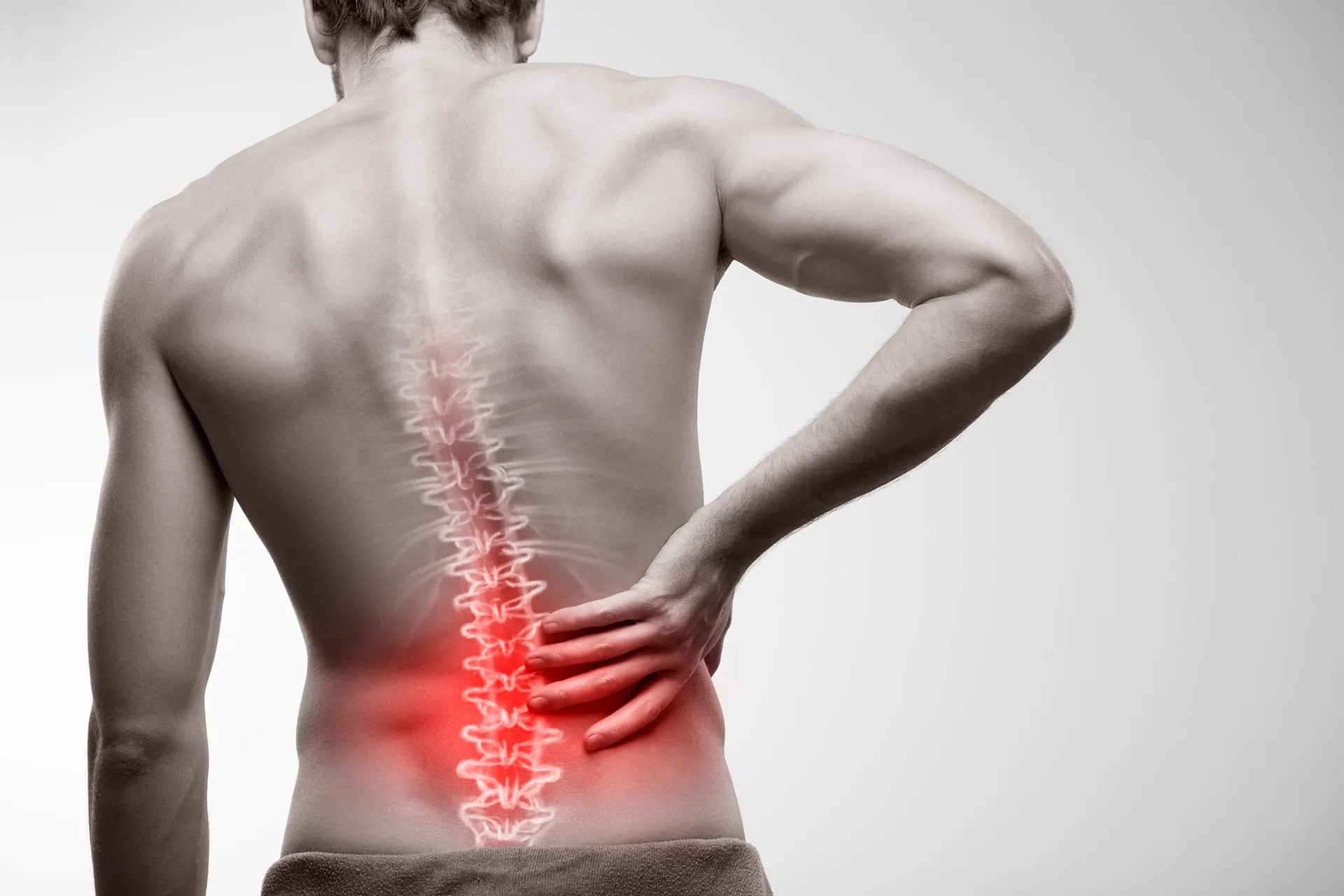 Man from behind holding his lower back, the lumbar spine shown in red