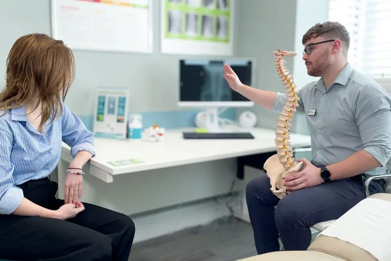 Chiropractor explaining a care plan with a spine model before treatment starts