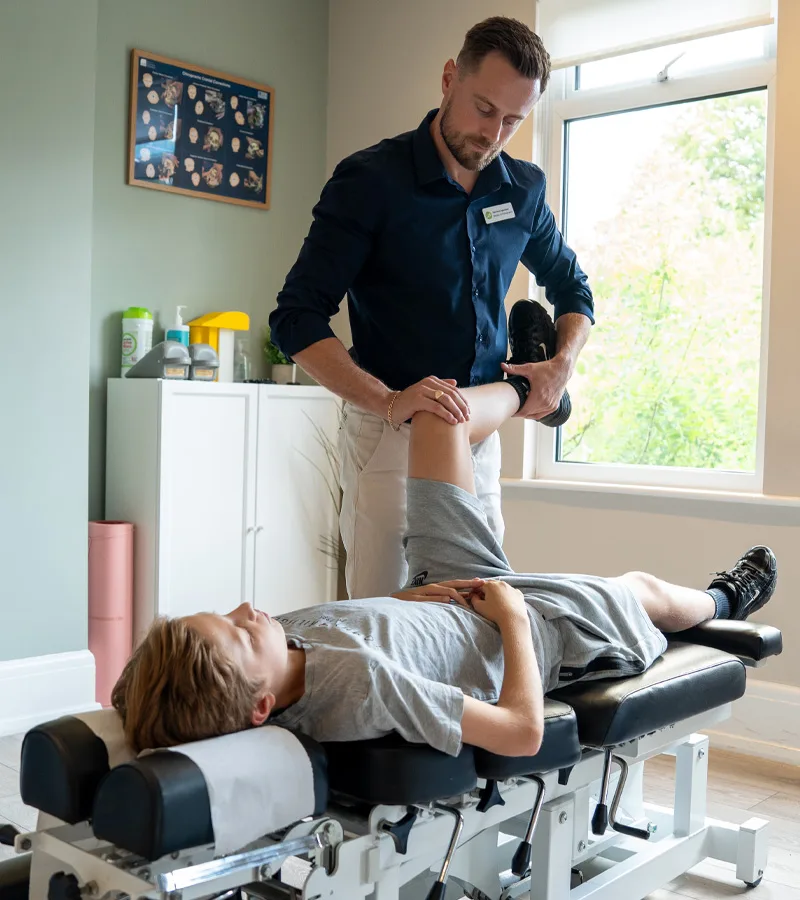 Chiropractor assessing the hip and leg of a patient on a treatment table