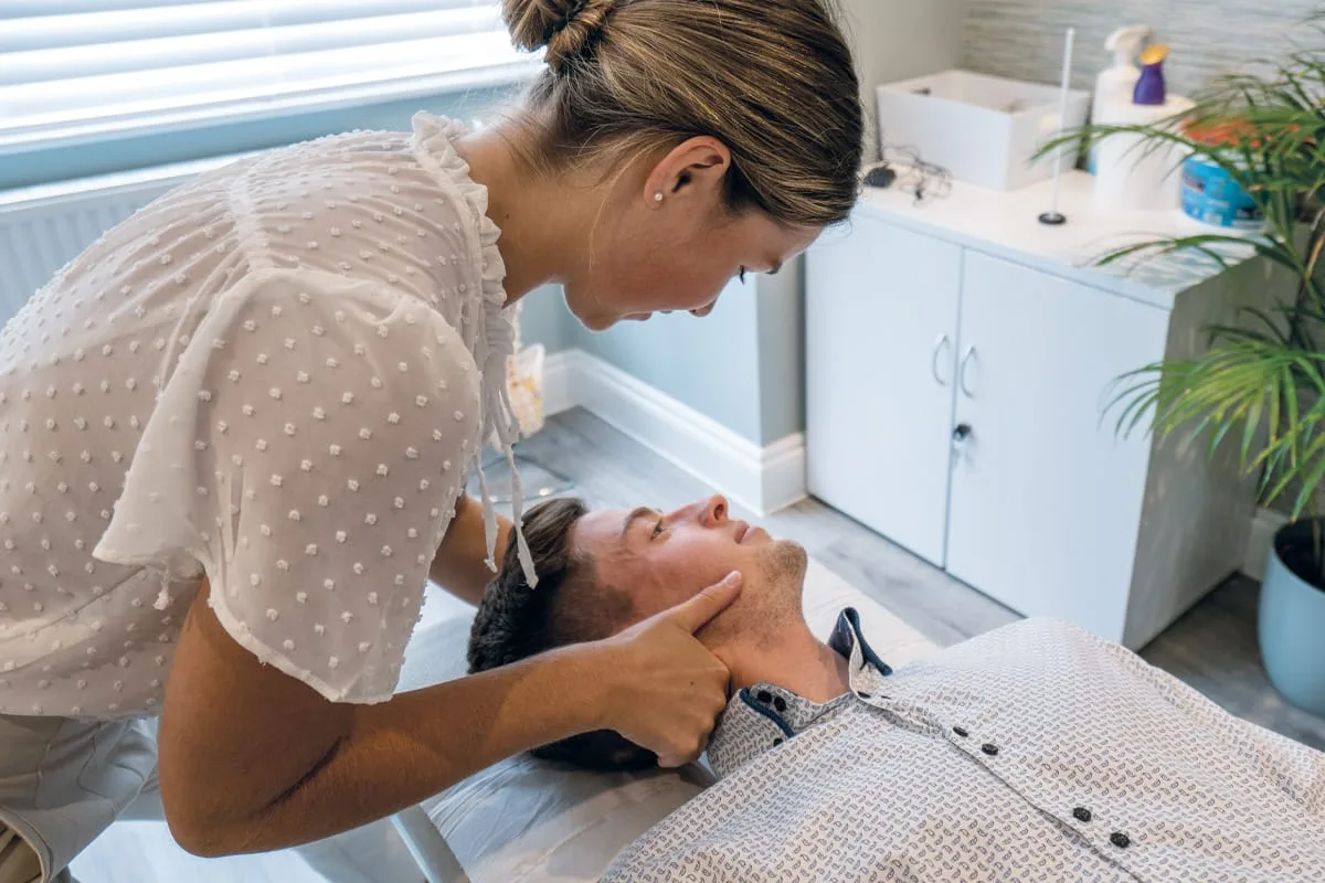 Chiropractor gently assessing the neck of a patient lying face up