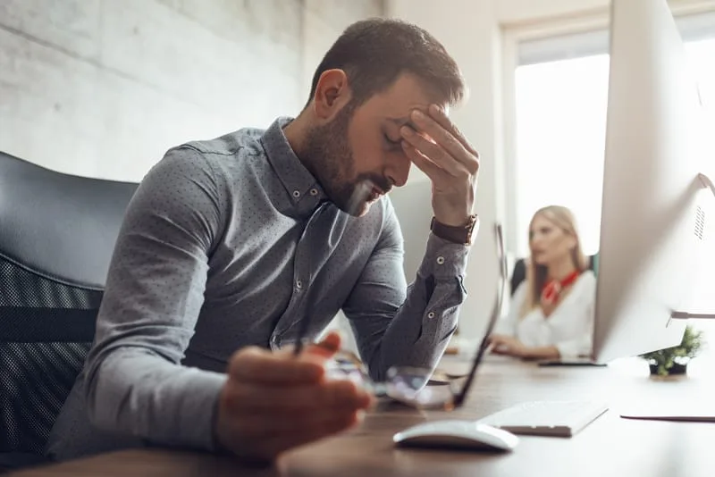Man at a desk holding his forehead