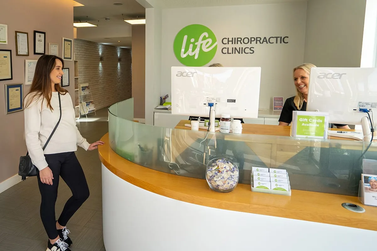 Curved Life Chiropractic reception desk with the green logo on the wall